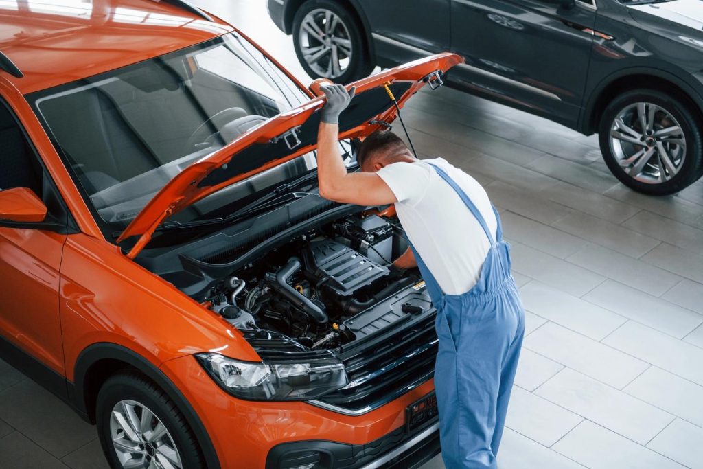 Mechanic inspecting orange car engine during used car inspection services in Houston showroom.