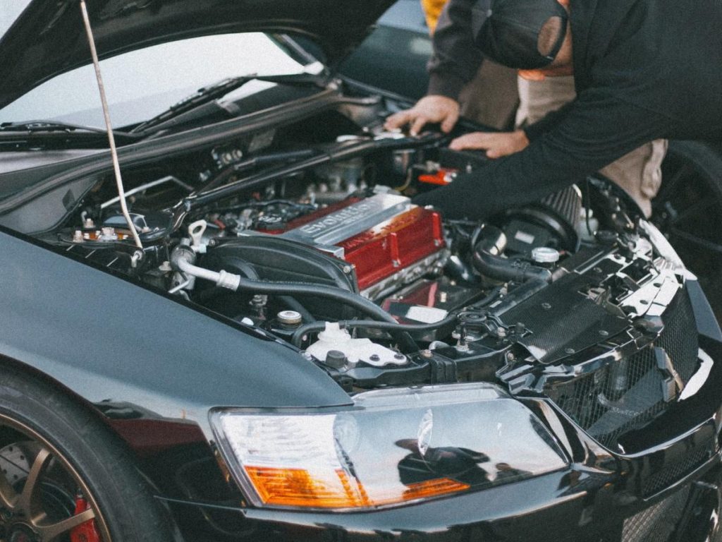 Mechanic inspecting a car's engine during Used Auto Inspection Houston, with hood open and tools in use.
