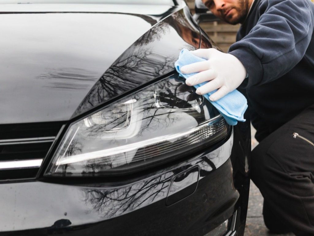 Mechanic polishing a black car's hood during Used Auto Inspection Houston, using a blue cloth and gloves.