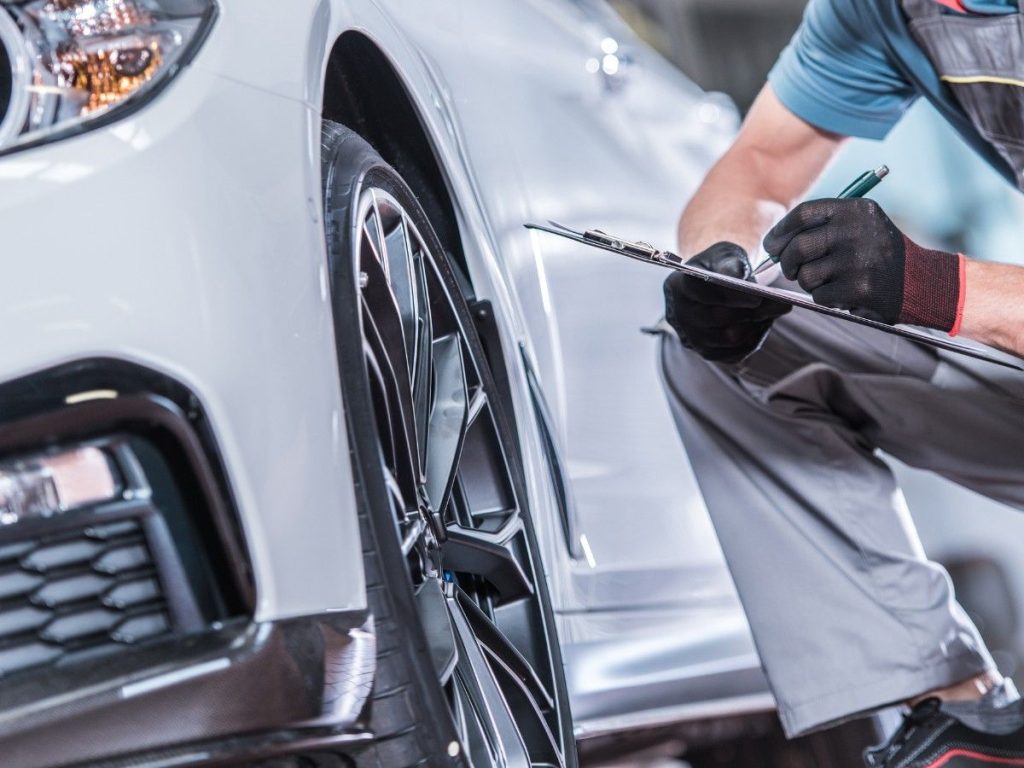 Technician checking tires on a silver sedan during Used Auto Inspection Houston, with a lift and tools in the background.