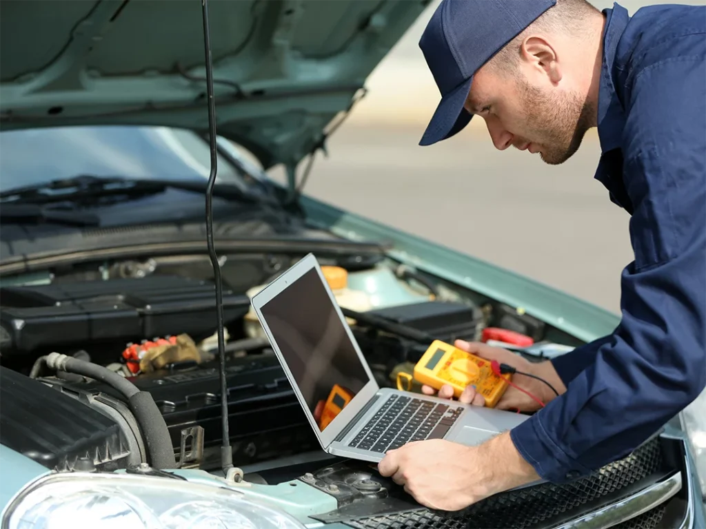 Mechanic using laptop and multimeter for check used car service in Houston on an open car hood.