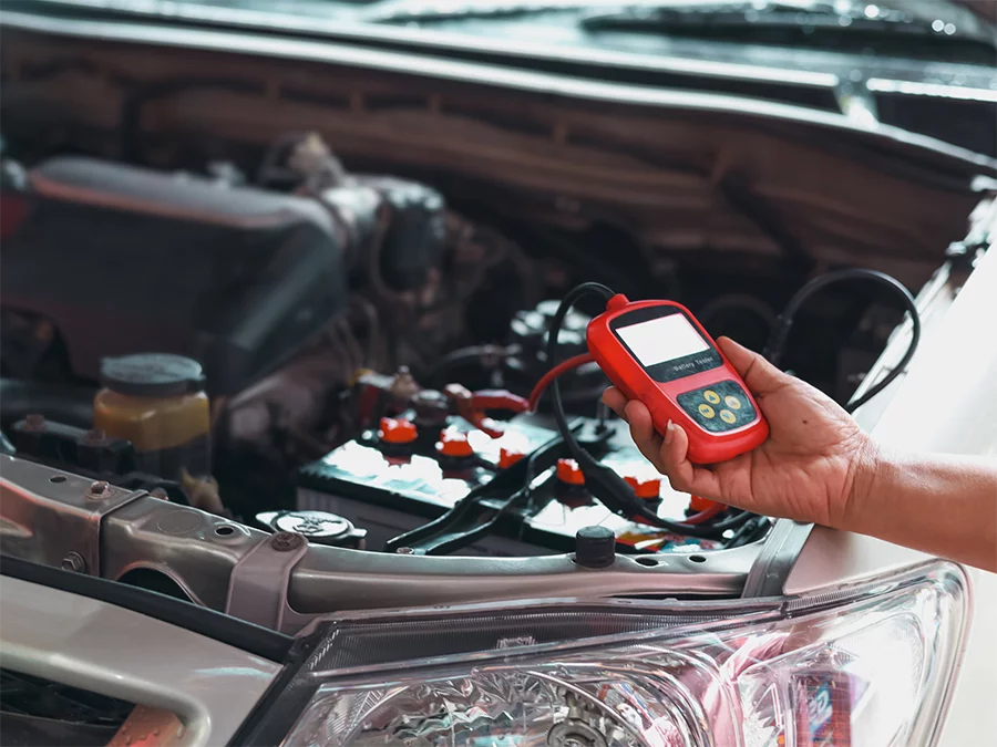 Hand using a battery tester for check used car service in Houston on an open car hood.