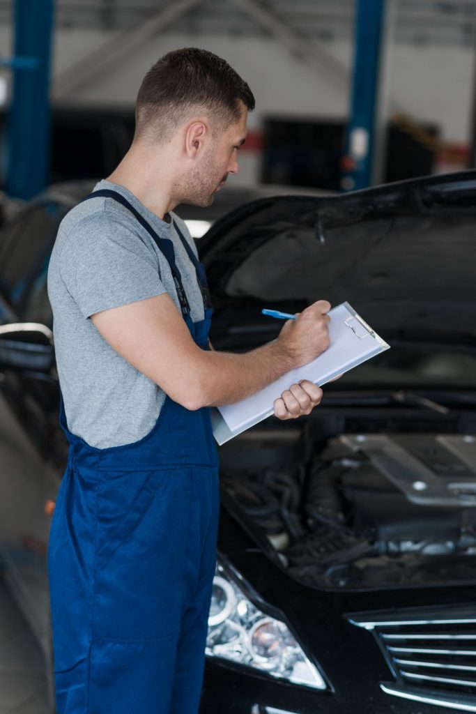 Mechanic performing third party inspection with checklist beside car engine.