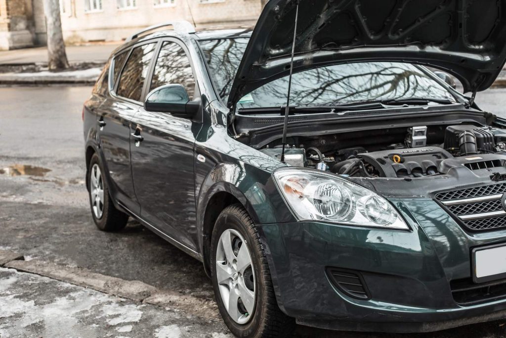Green car with open hood on roadside needing used car inspection services in Houston.