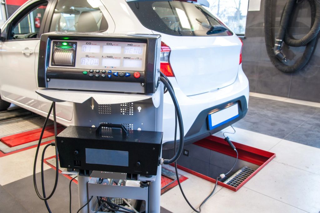 Technician performing check used car service Houston with diagnostic equipment on a white vehicle in a garage.