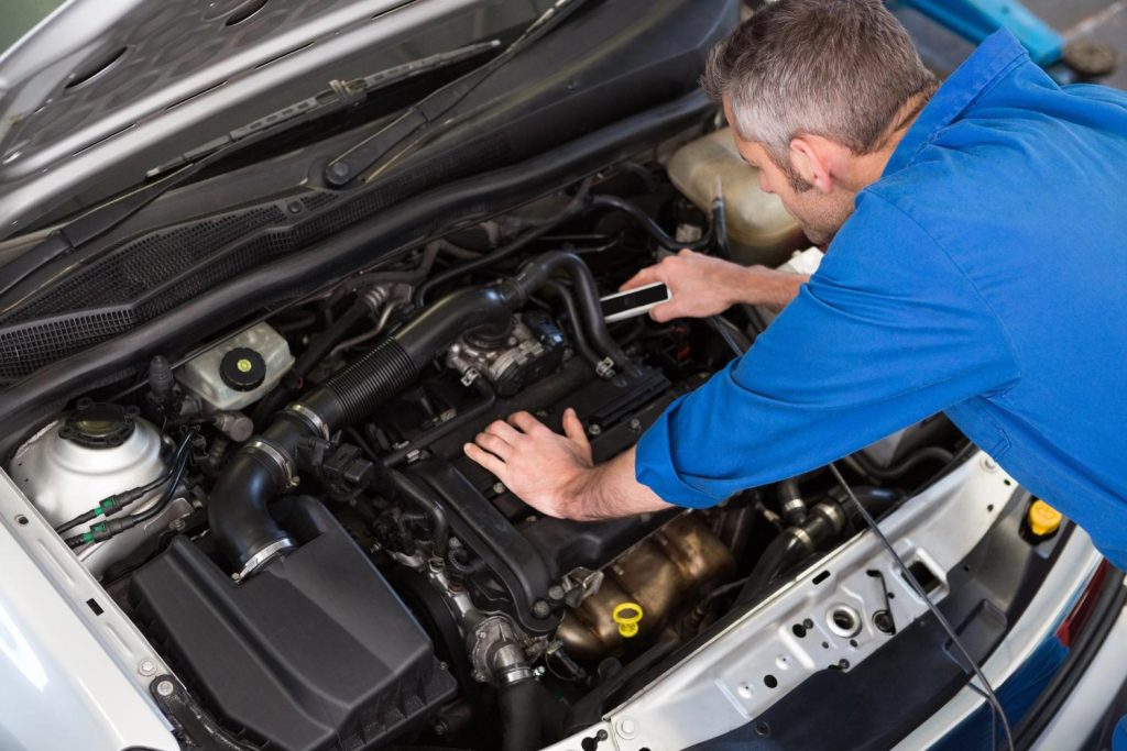 Mechanic inspecting car engine during used car inspection services in Houston garage.
