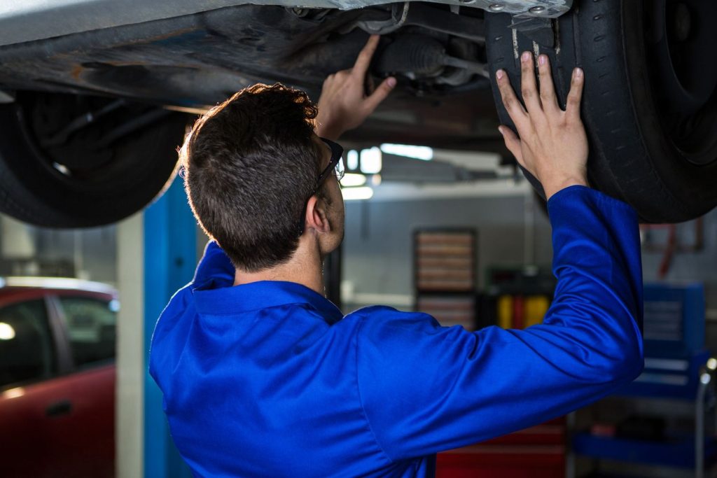 Mechanic inspecting car undercarriage during used auto inspection in Houston garage.