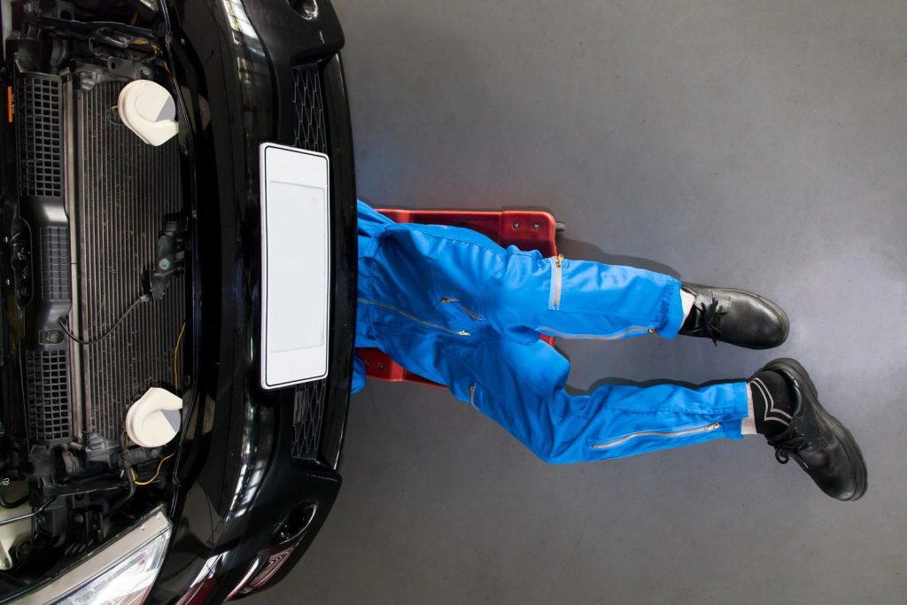 Mechanic under car checking engine during used car inspection services in Houston garage.
