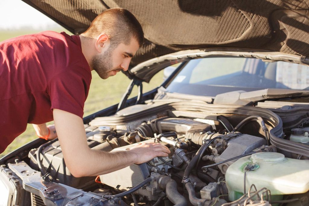 Man inspecting car engine during third party inspection in Houston outdoors.