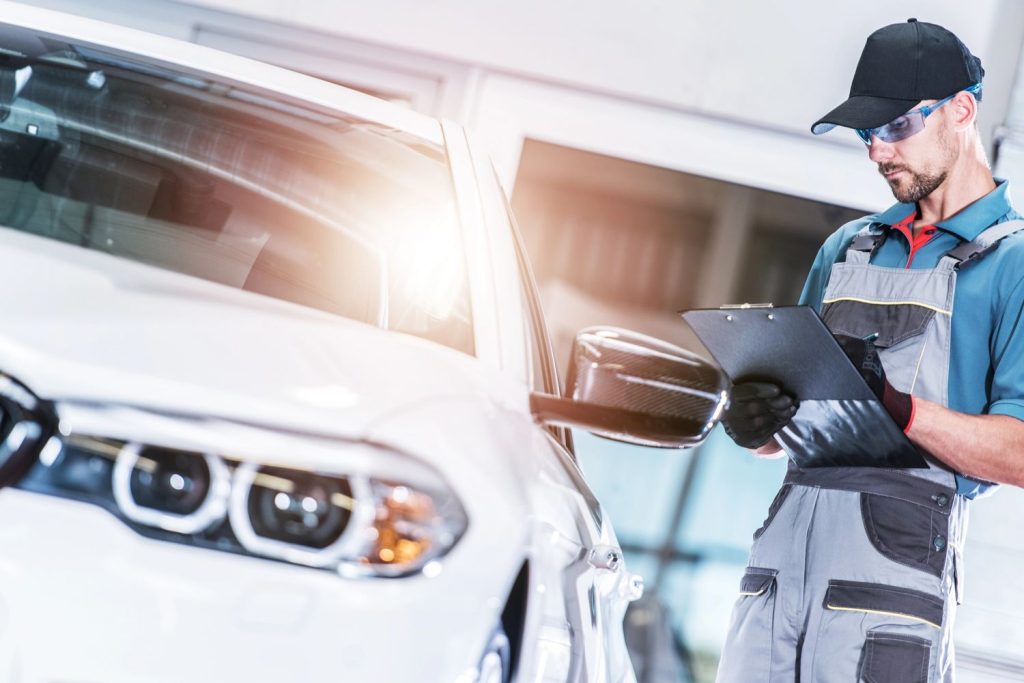 Mechanic inspecting car with clipboard for used car inspection services Houston.