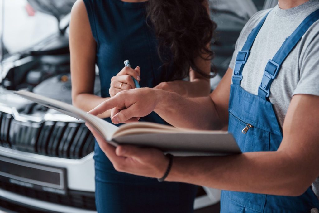 Mechanic and client reviewing car manual for Pre Purchase Inspection Houston, checking engine details thoroughly.