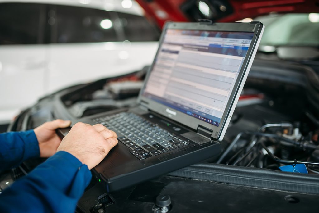 Close-up of a certified third party car inspector performing diagnostic checks on a car engine using a laptop.