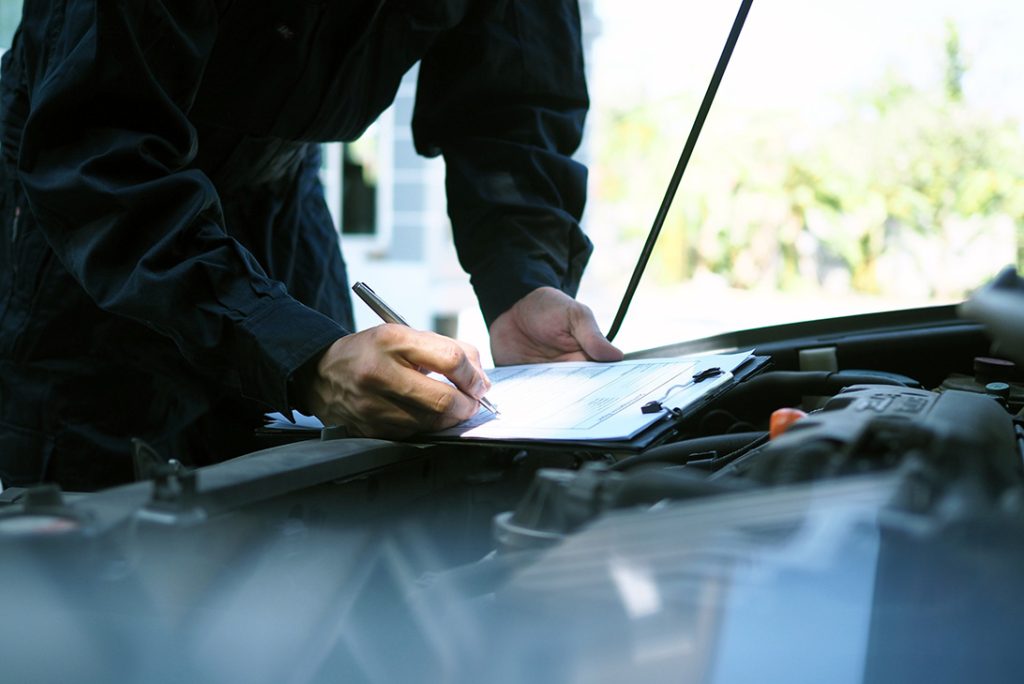 Technician writing notes on the clipboard during an on-site mobile car check Houston engine inspection.