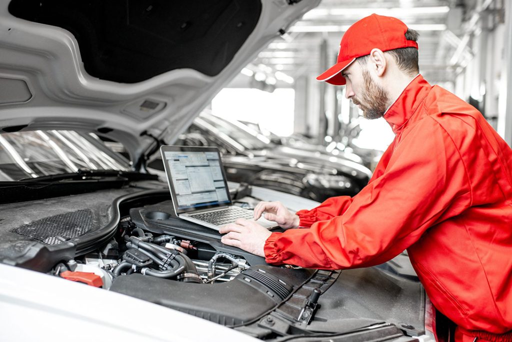 Mechanic using a laptop for digital engine checks during a same day pre purchase car inspection.