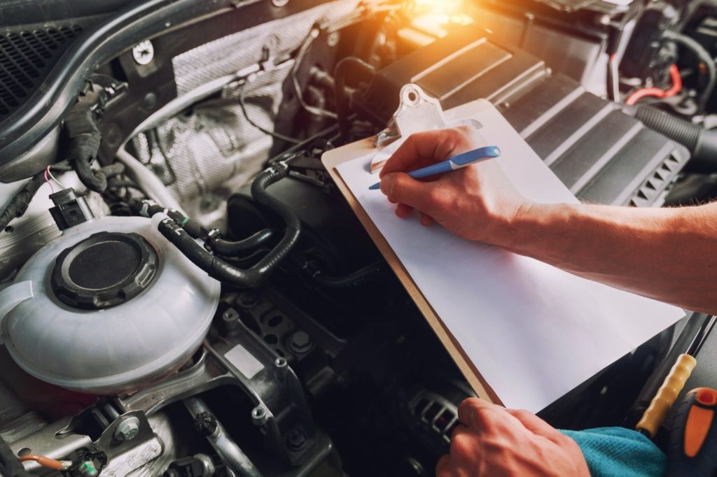 Best car inspection service Houston: Technician writing notes during a detailed engine and fluid level check.