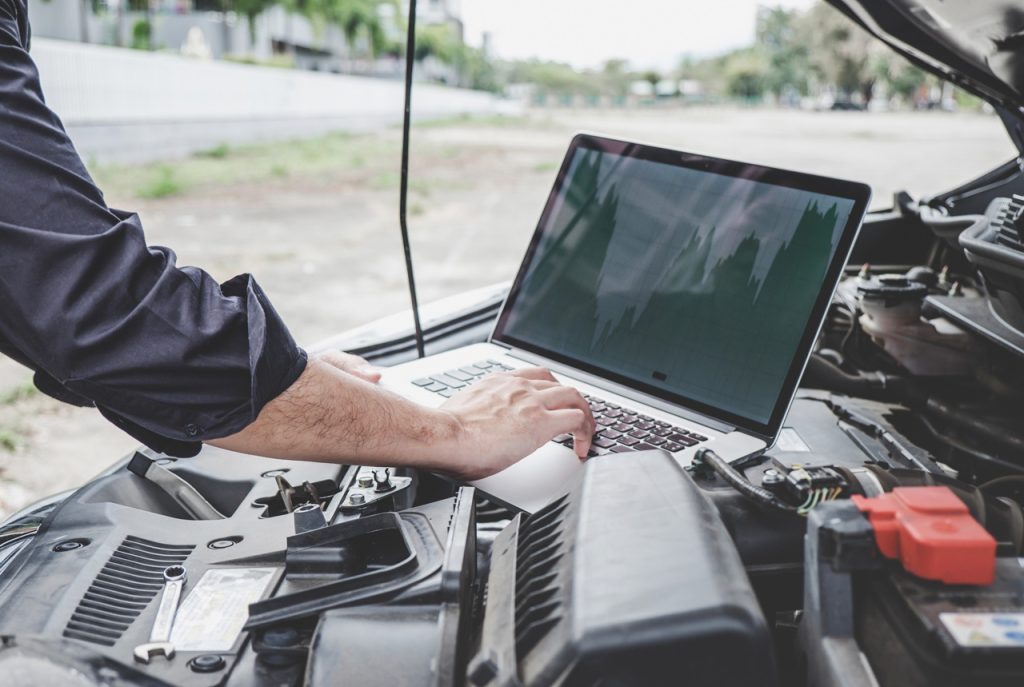 Technician using a laptop to check used car service Houston records and perform advanced engine computer diagnostics.