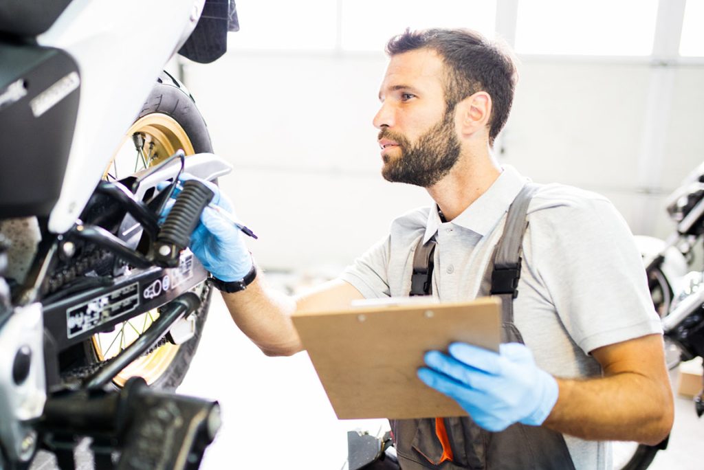 Expert technician performing a frame check on a motorcycle for a comprehensive on-site used car inspection service.