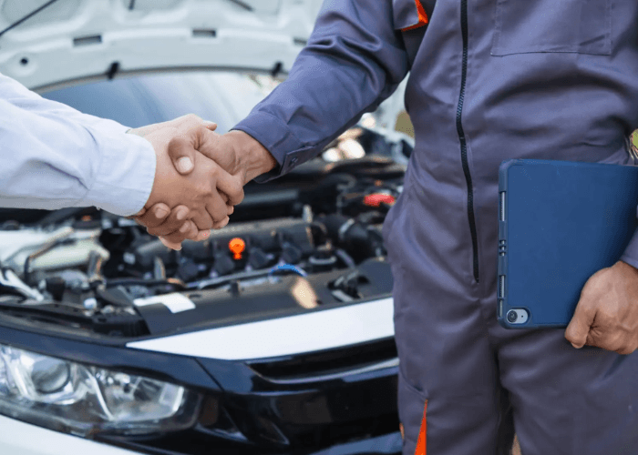 Buyer and mechanic shaking hands after a successful third party vehicle inspection before purchase by the open car hood.